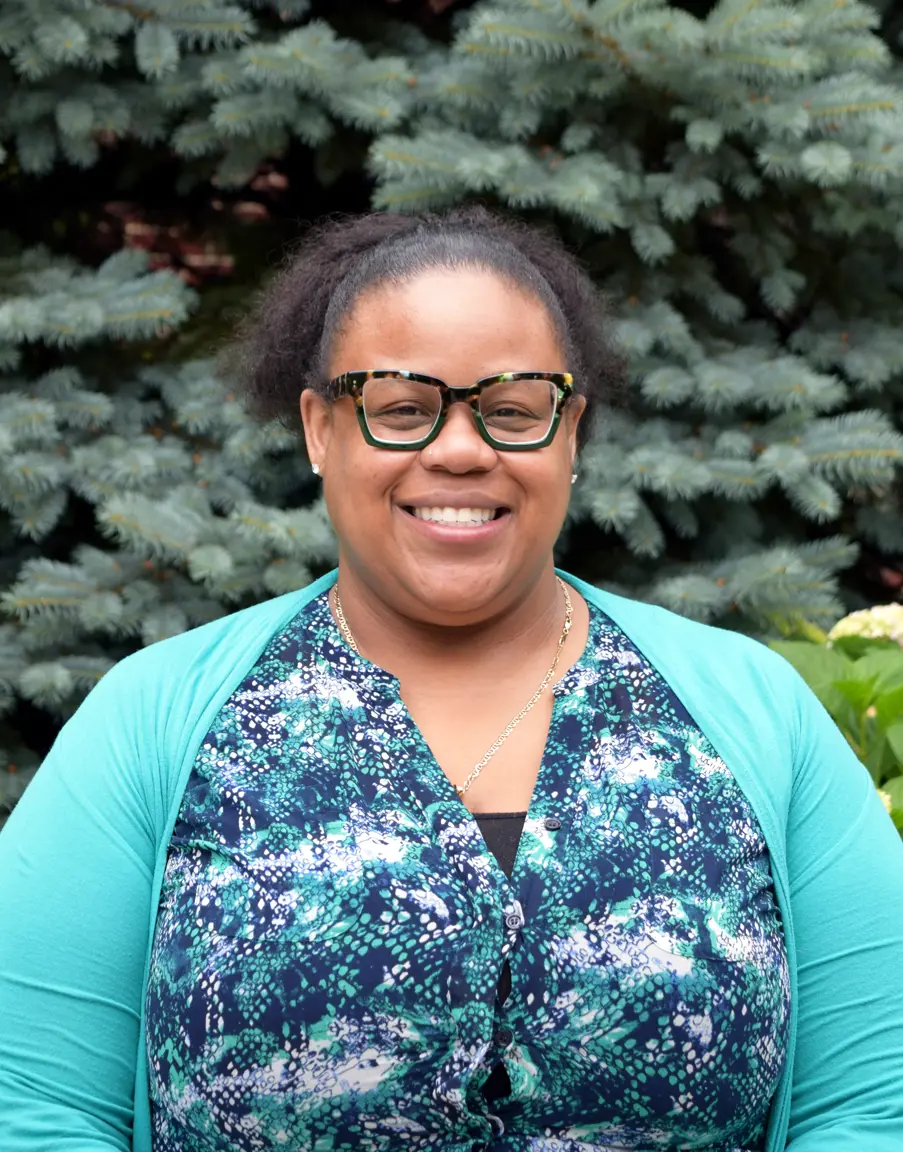 A headshot of Registrar Nicole Martinez standing in front of an evergreen tree and smiling. 